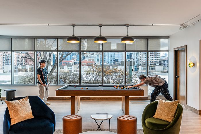 Chic apartment lounge featuring a stylish pool table, cozy seating, and large windows with vibrant urban views.