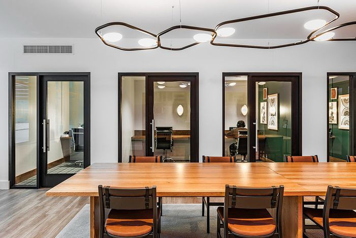 Modern meeting room with elegant wooden table, stylish lighting, and glass-enclosed private offices in a sleek workspace.
