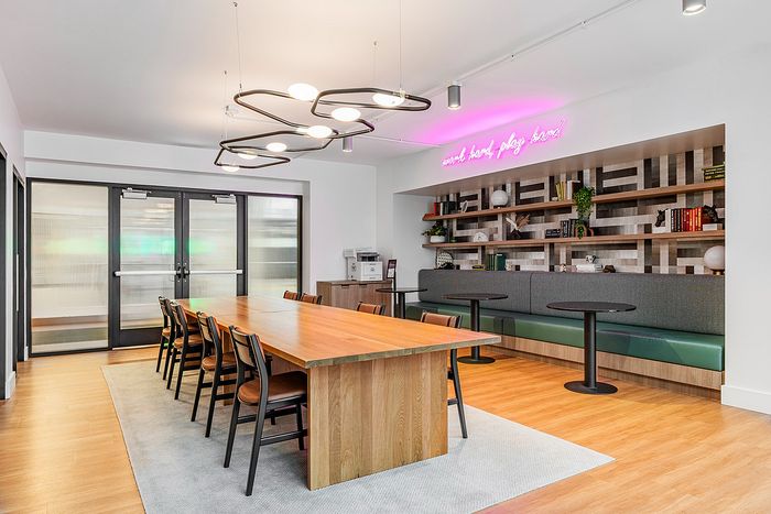 Modern and inviting meeting room with a large wooden table, stylish chairs, and a neon sign above cozy seating area.
