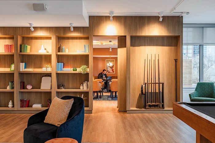 Chic lounge area with modern wooden bookshelf, cozy armchair, and billiards setup, leading to a stylish dining space.