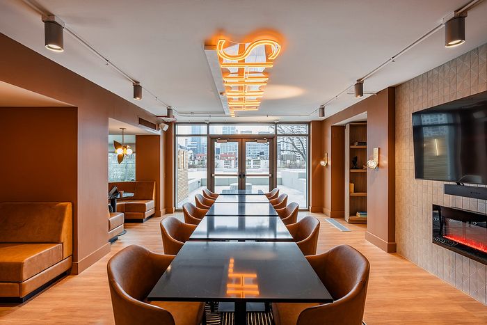 Modern communal lounge with stylish furnishings, large conference table, and vibrant city view through glass doors.