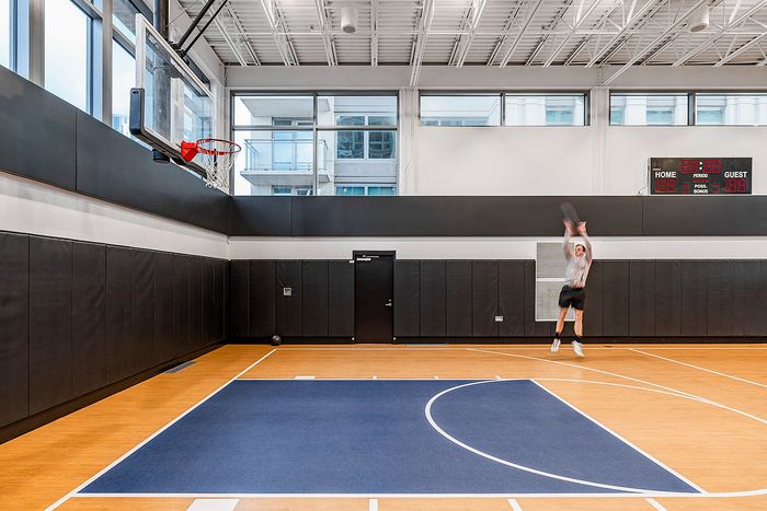 Modern indoor basketball court with sleek design and natural lighting, featuring a player making a jump shot.