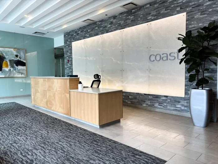 Modern apartment lobby with sleek wooden reception desk, stylish stone accent wall, and abstract art, offering a welcoming and chic atmosphere.