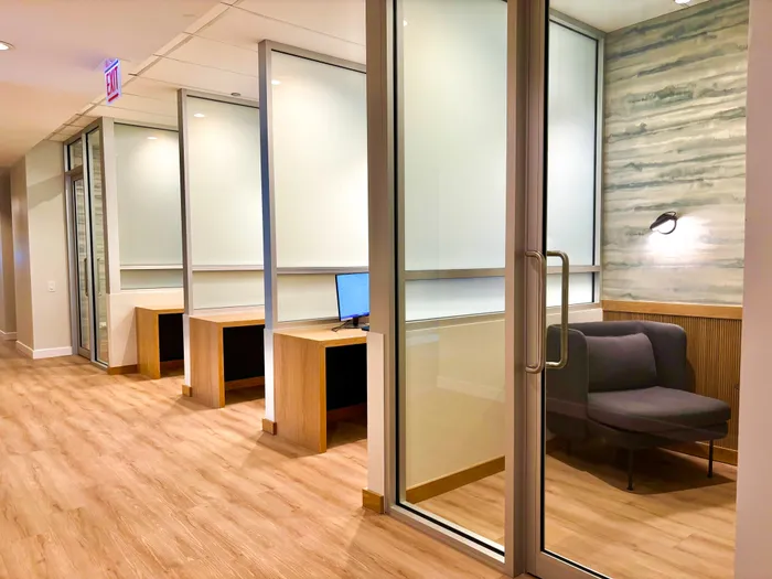 Modern office space featuring sleek glass partitions, stylish wooden desks, and a cozy seating area with elegant lighting.