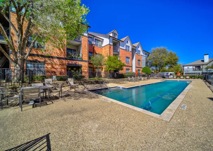 Charming apartment complex with a refreshing pool, surrounded by lush greenery and stylish seating areas, perfect for relaxation and social gatherings under a clear blue sky.