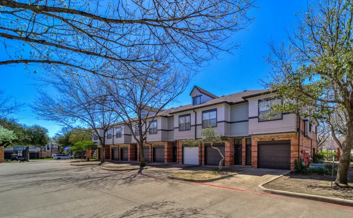 Charming townhouse complex with elegant brick accents and lush surroundings under a clear blue sky.