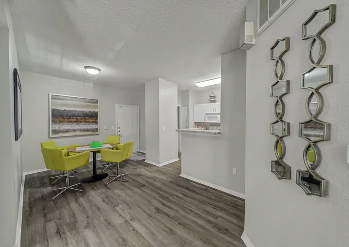 Modern apartment interior showcasing an inviting dining area with bright green chairs, elegant artwork, and sleek wood flooring leading to a cozy kitchen.
