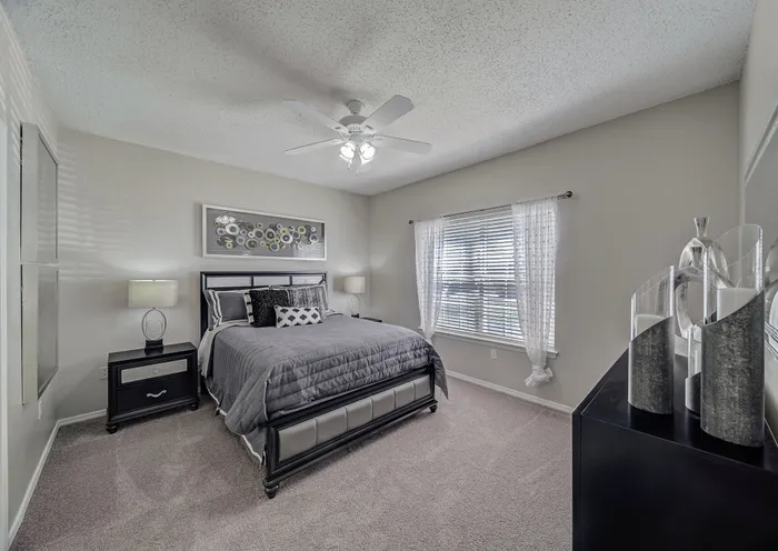 Inviting bedroom with modern decor, featuring plush carpeting, elegant bedside lamps, and abundant natural light through large windows.
