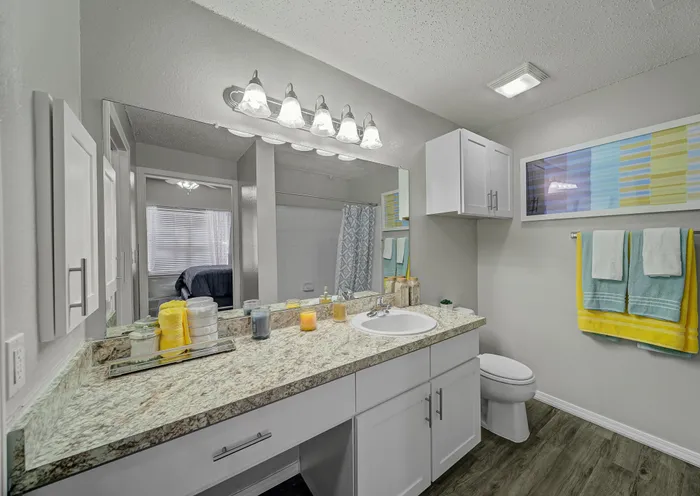Modern bathroom with elegant granite countertop, stylish lighting, and vibrant towels, offering a fresh and inviting ambiance.