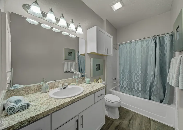 Modern bathroom featuring a granite countertop with integrated sink, stylish lighting, and elegant blue patterned shower curtain.