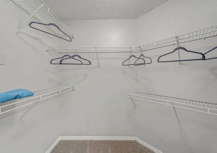 Spacious walk-in closet with sleek white shelving and multiple hangers, perfect for ample storage and organization.