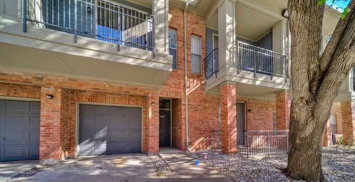 Charming suburban residence featuring red brick facade, dual garages, and sunlit balconies overlooking a tree-lined driveway.