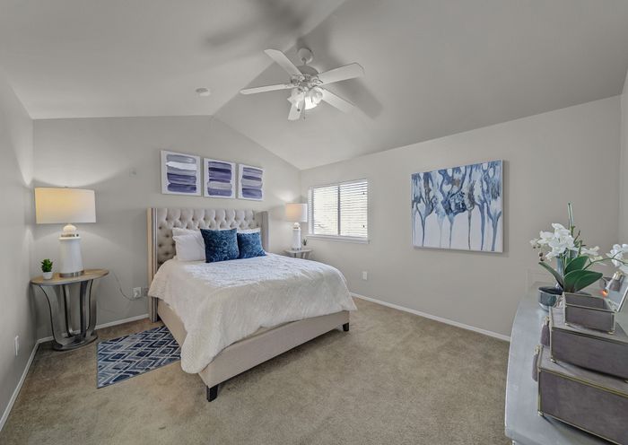 Elegant bedroom with vaulted ceiling, featuring a plush bed with white bedding and blue accent pillows, modern decor, and a large window filling the space with natural light.