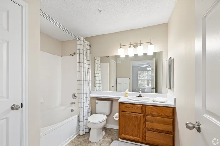 Bright, inviting bathroom featuring a modern vanity with wood cabinets, large mirror, and elegant overhead lighting. Includes a pristine bathtub with a stylish shower curtain.