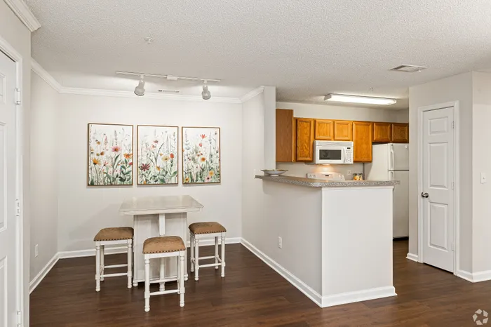 Charming apartment kitchen with wood cabinets, sleek countertops, and a cozy dining area featuring floral artwork.