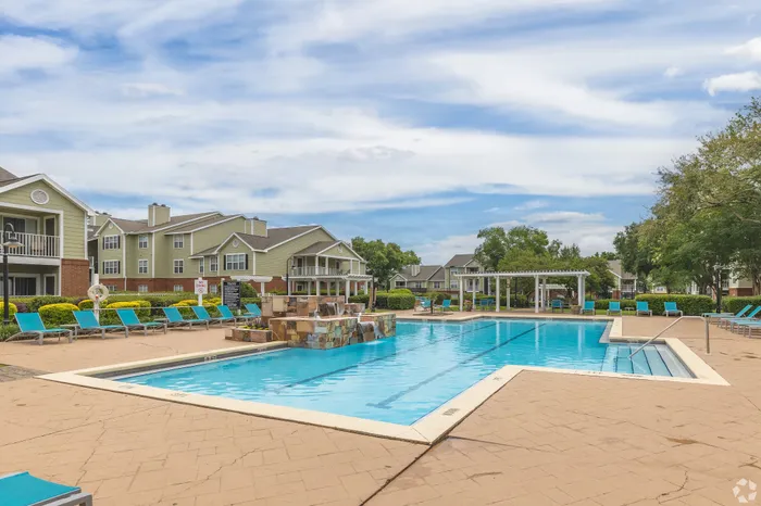Luxurious apartment complex with a sparkling outdoor pool, sun loungers, and lush landscaping for a resort-style living experience.