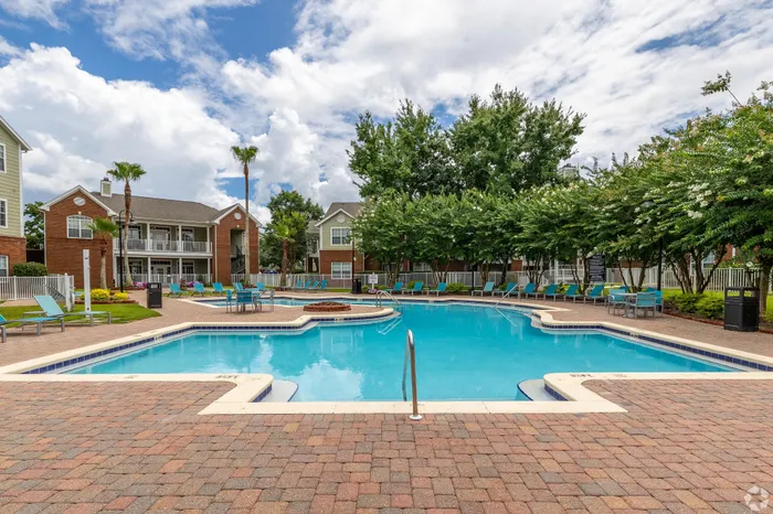 Inviting apartment community pool area surrounded by lush greenery and stylish loungers, perfect for relaxation and recreation.