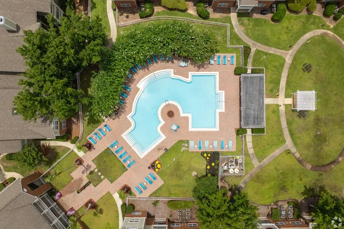 Aerial view of luxurious apartment complex featuring a stunning resort-style pool with surrounding sun loungers, lush greenery, and elegant pathways.