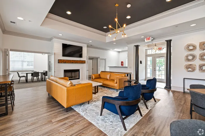 Modern and inviting apartment lobby with stylish orange leather sofas, dark blue armchairs, and sleek wooden flooring, perfect for relaxation and social gatherings.