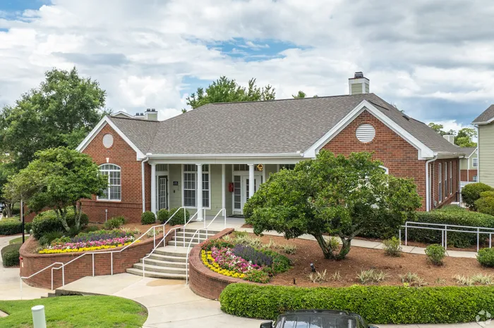Charming brick community center surrounded by lush greenery and vibrant flower beds, offering a welcoming entrance with neatly paved pathways.