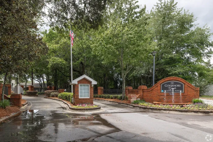 Inviting entrance to Governors Gate Apartments, featuring lush greenery and a welcoming brick design.