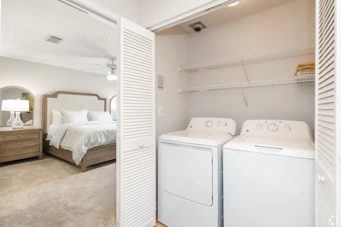 Bright bedroom with cozy queen bed and spacious in-unit laundry area with modern washer and dryer.