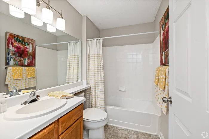 Charming bathroom with modern fixtures, vibrant art, and cozy yellow accents.