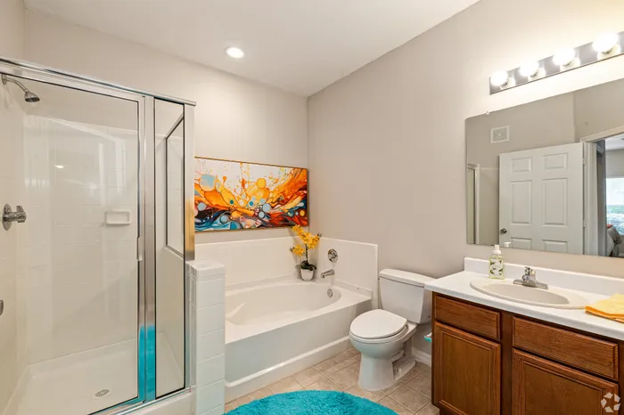 Modern bathroom with sleek glass shower, bathtub, vibrant artwork, and elegant vanity.