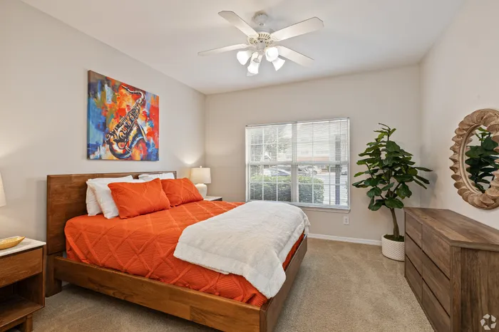 Bright and cozy bedroom featuring a stylish wooden bed with vibrant orange bedding, complemented by a colorful saxophone artwork above, a lush indoor plant, and elegant light fixtures.