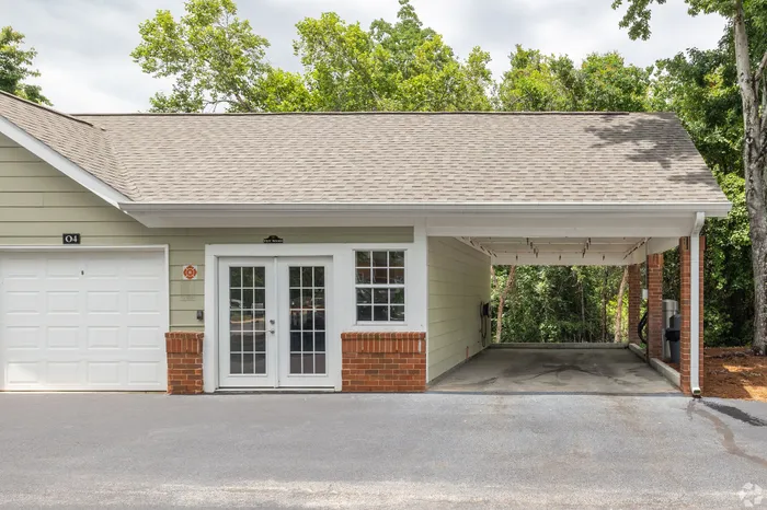 Charming garage featuring stylish French doors and a covered carport, surrounded by lush greenery.
