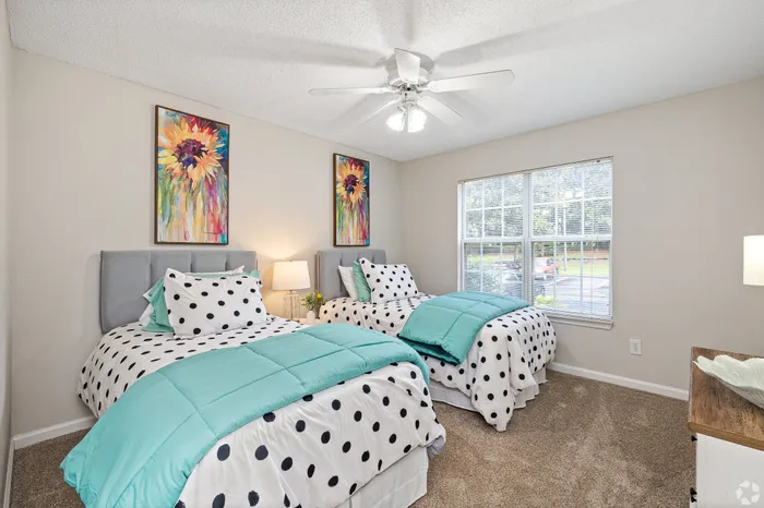 Bright and stylish bedroom with two twin beds, accented by colorful artwork and polka dot bedding, featuring ample natural light from a large window.