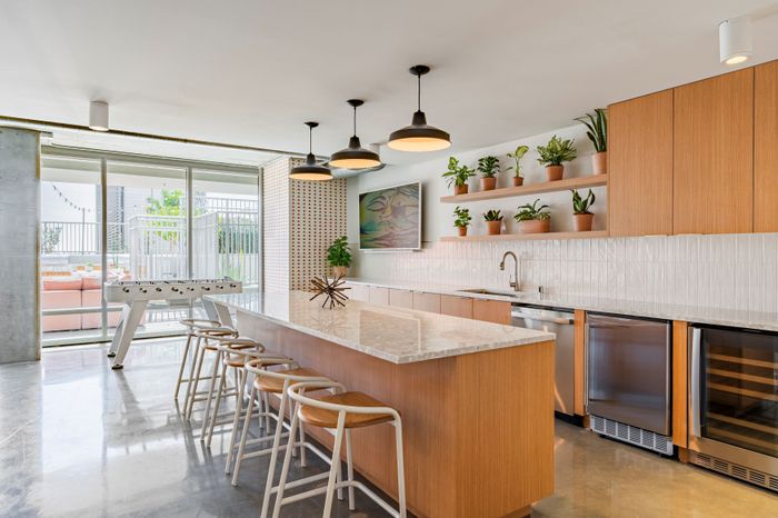 Bright modern kitchen featuring a sleek marble island with bar seating, stylish pendant lighting, and abundant natural light from large glass doors. Indoor plants add a touch of greenery to this inviting space.