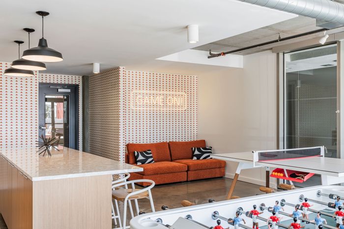 Contemporary game room with stylish orange couch, playful wall art, and foosball and ping pong tables, offering a vibrant entertainment space.