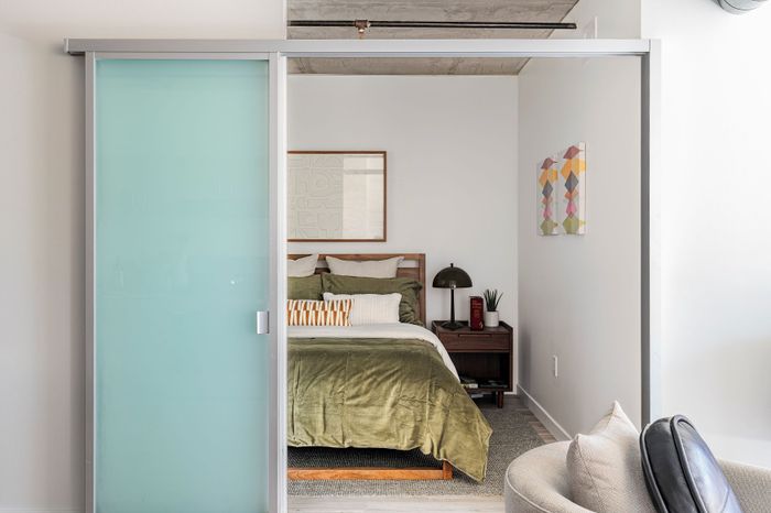 Modern bedroom with a cozy olive green bed, stylish frosted glass sliding door, and elegant decor, creating a serene and inviting atmosphere.