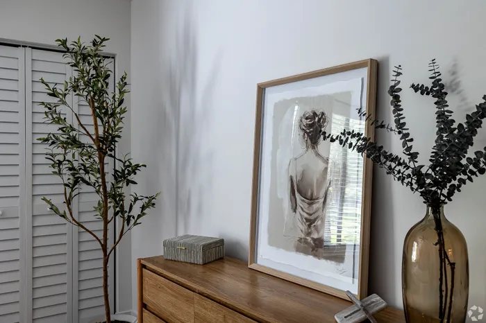 Elegant interior design featuring a wooden dresser with stylish framed artwork, lush indoor plants, and modern decor accents.