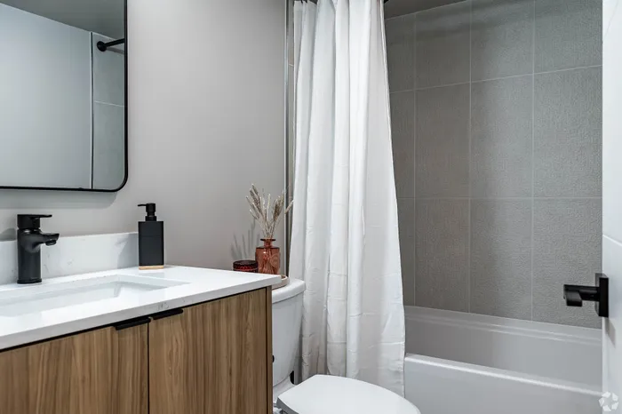 Modern bathroom with sleek vanity, elegant black fixtures, and a pristine white shower curtain, offering a serene and stylish atmosphere.
