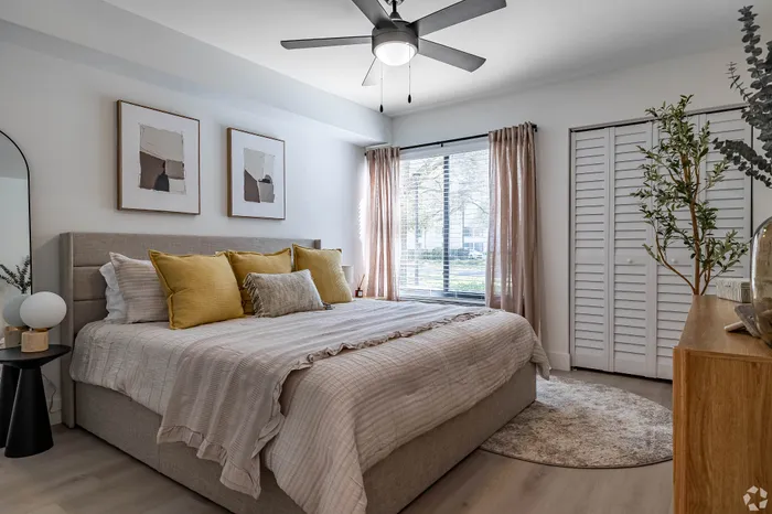 Bright and inviting bedroom with large window, stylish artwork, and plush bed adorned with yellow accents.