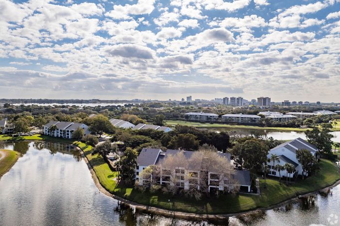 Scenic aerial view of a picturesque apartment community surrounded by lush greenery and serene water, offering a blend of tranquility and urban convenience.
