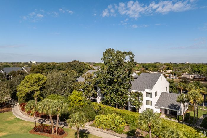 Scenic aerial view of a charming white residence surrounded by lush greenery and palm trees, offering a serene and idyllic living environment.