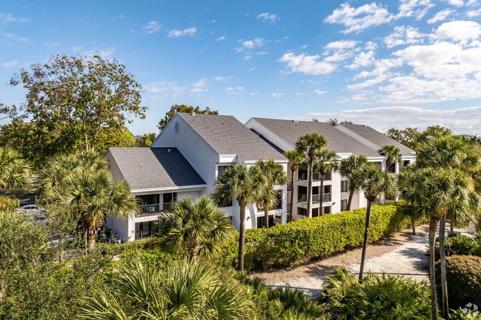 Charming apartment complex surrounded by lush palm trees, highlighting modern architecture and serene pathways under a bright blue sky.