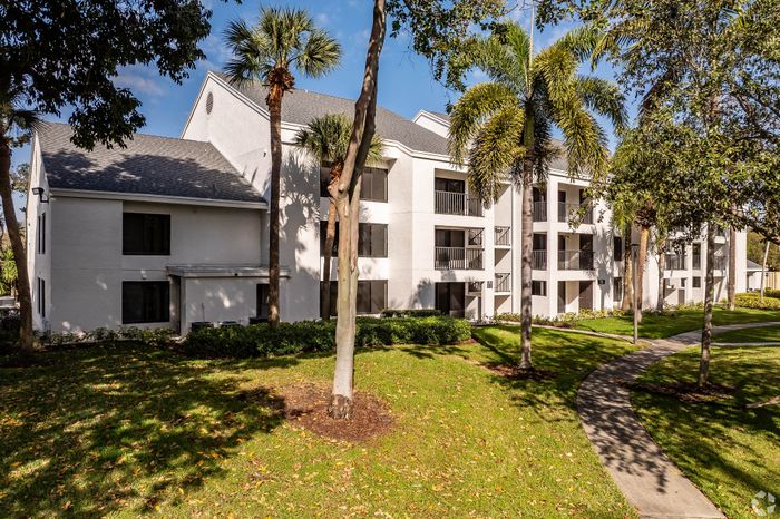 Charming apartment building nestled among lush palm trees, featuring modern white exterior and inviting pathways.