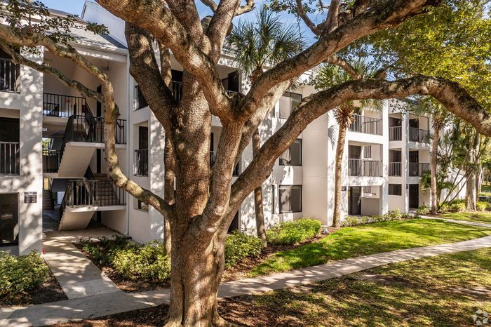 Charming apartment complex with modern architecture, surrounded by lush greenery and shaded walkways, perfect for serene living.
