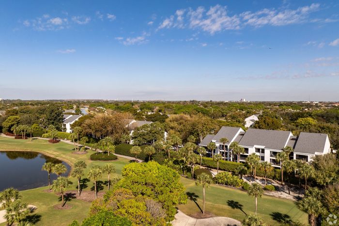 Breathtaking aerial view of a serene residential community surrounded by lush greenery and a tranquil pond, offering an idyllic living environment.