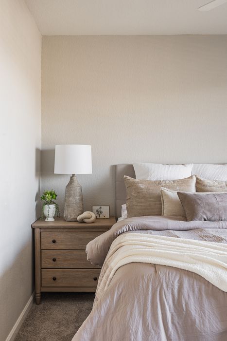Elegant bedroom corner featuring a cozy bed with plush pillows and a stylish wooden nightstand adorned with a chic lamp and vibrant greenery.