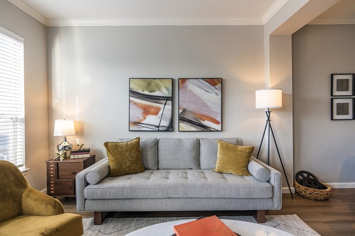 Elegant living room featuring a modern gray sofa with mustard pillows, contemporary abstract art, and stylish lighting in a cozy, sunlit setting.