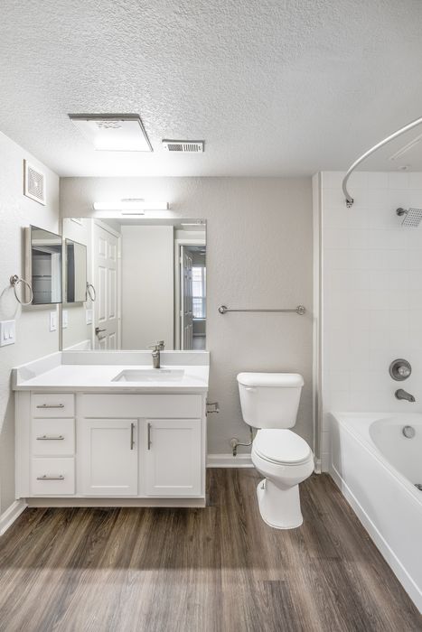 Modern bathroom featuring elegant white vanity, sleek mirror, and inviting bathtub set against a stylish wood floor.