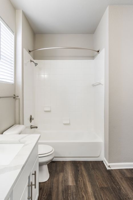 Modern bathroom with elegant white tiles, sleek shower, and rich wood flooring, boasting a bright and refreshing ambiance.