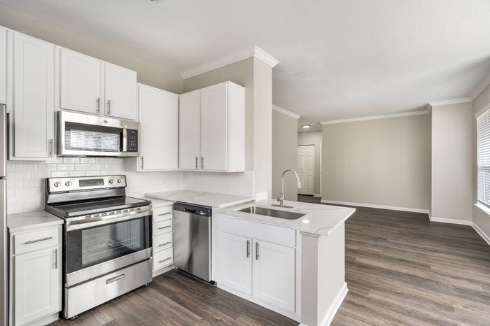 Modern kitchen with elegant white cabinetry, stainless steel appliances, and sleek hardwood floors opening to a spacious living area.