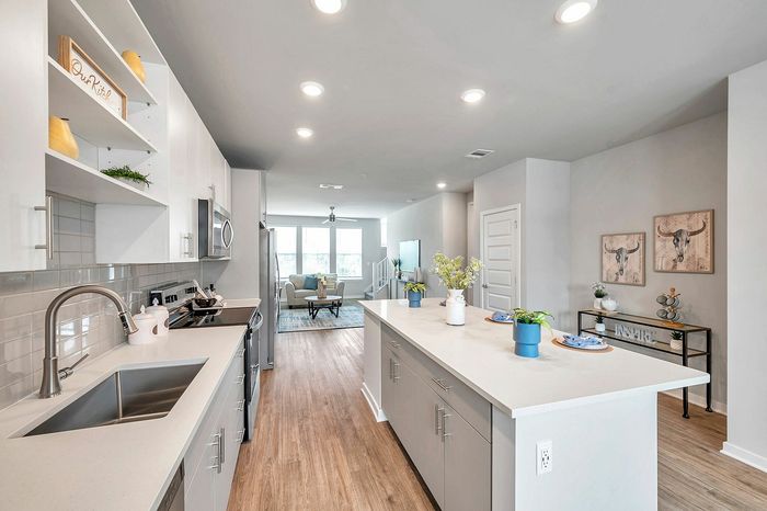 Modern kitchen with sleek countertops, stainless steel appliances, and open layout leading to a bright living room. Stylish decor and ample lighting create a warm, inviting atmosphere.