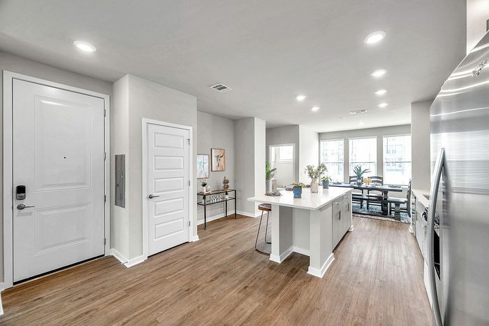Modern apartment interior with open-plan layout featuring a sleek kitchen island, stainless steel appliances, and bright dining area with large windows.
